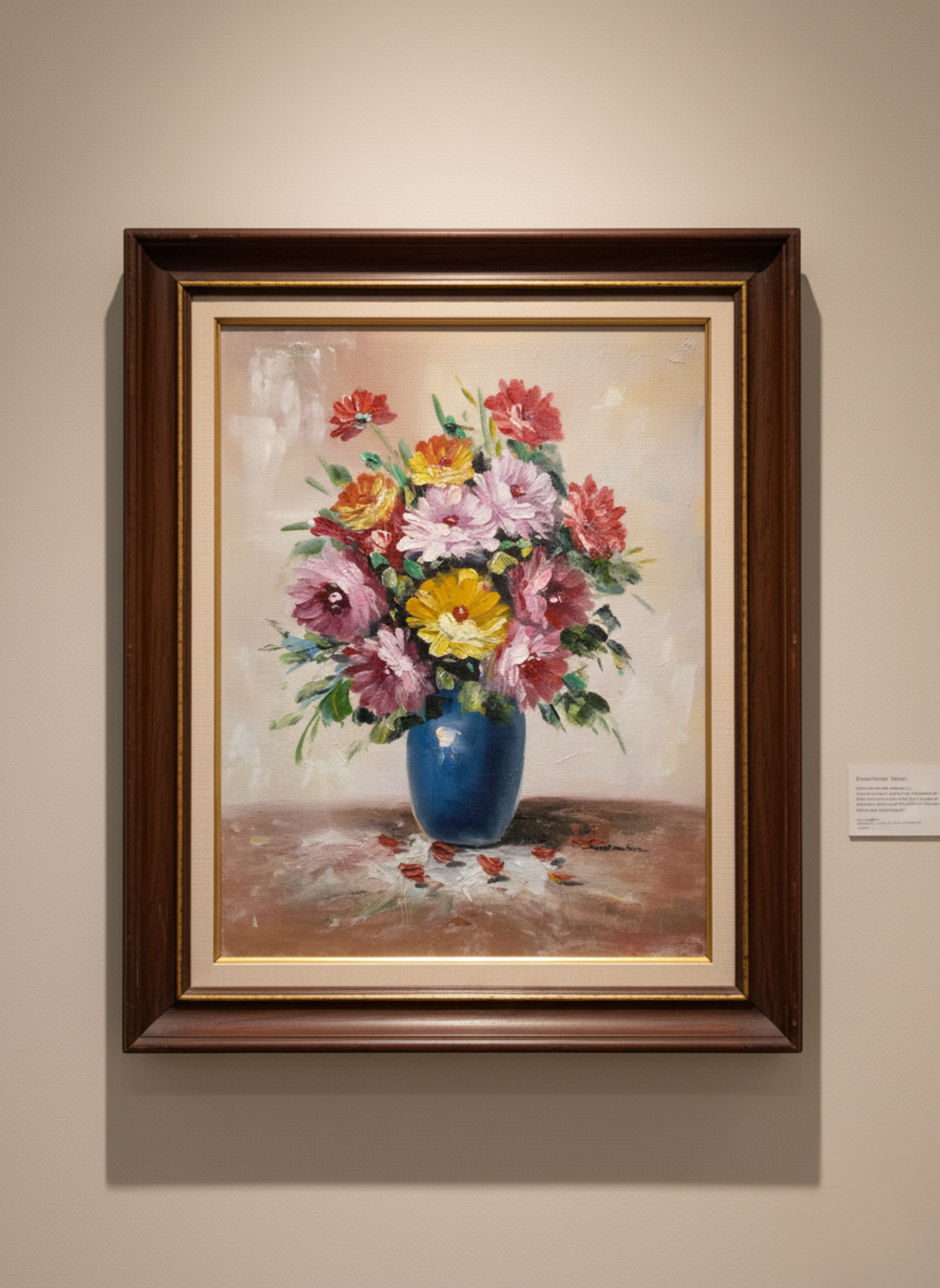 Framed painting of a bouquet of flowers in a blue vase on a beige wall.