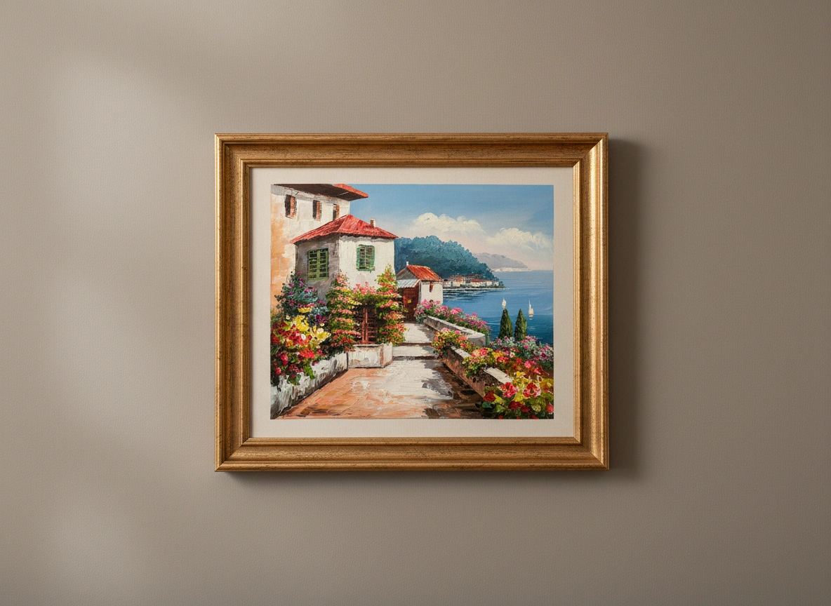 Framed painting of a coastal scene with a house and garden on a beige wall.