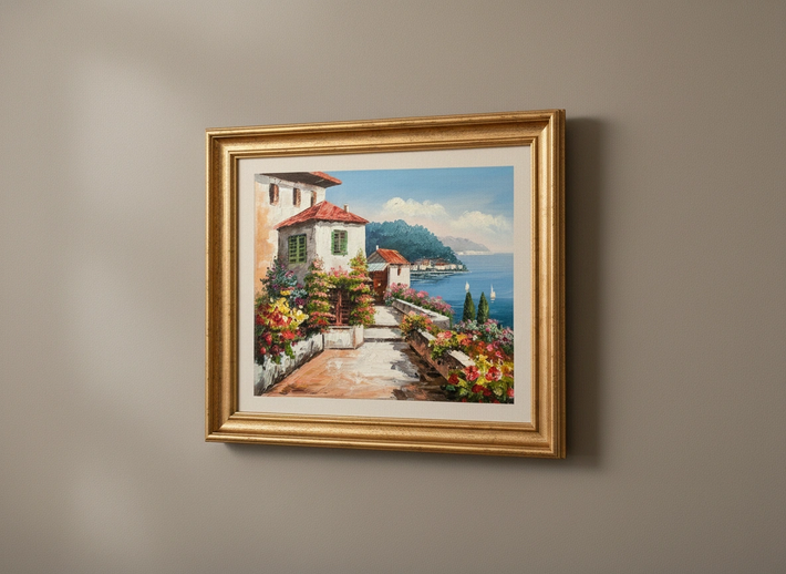 Framed painting of a coastal scene with flowers and a house on a wall.