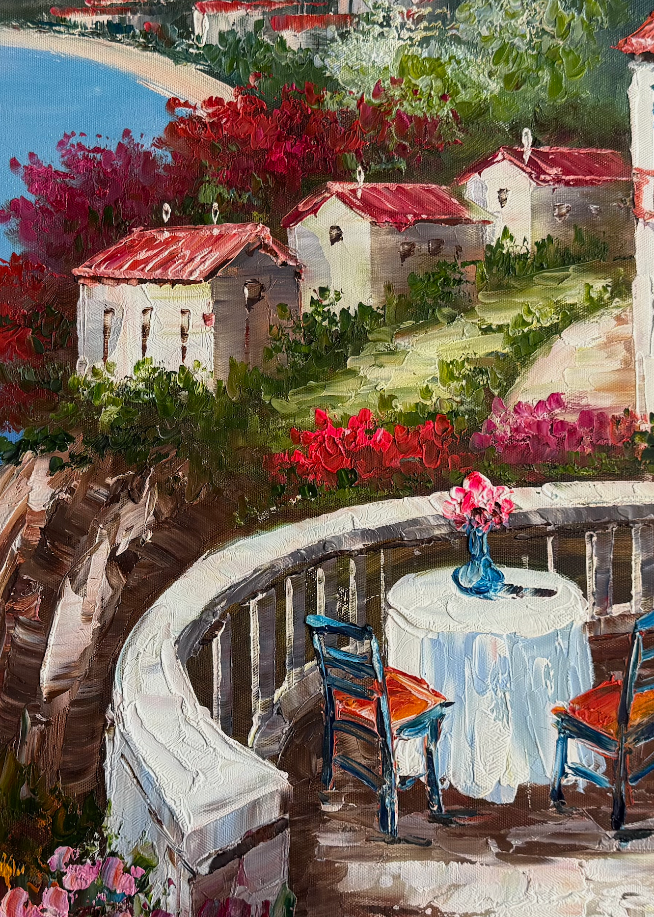 Painting of a scenic coastal village with a table and chairs on a balcony.